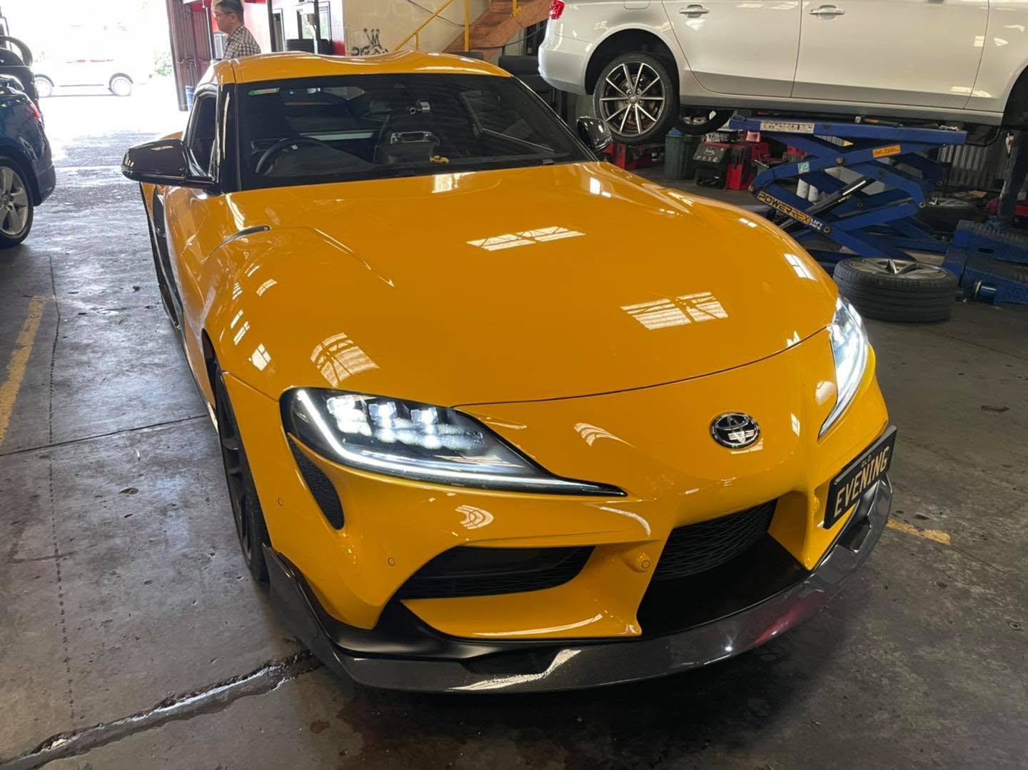 An orange sports car inside the Tyre Select workshop with another vehicle on a lift.